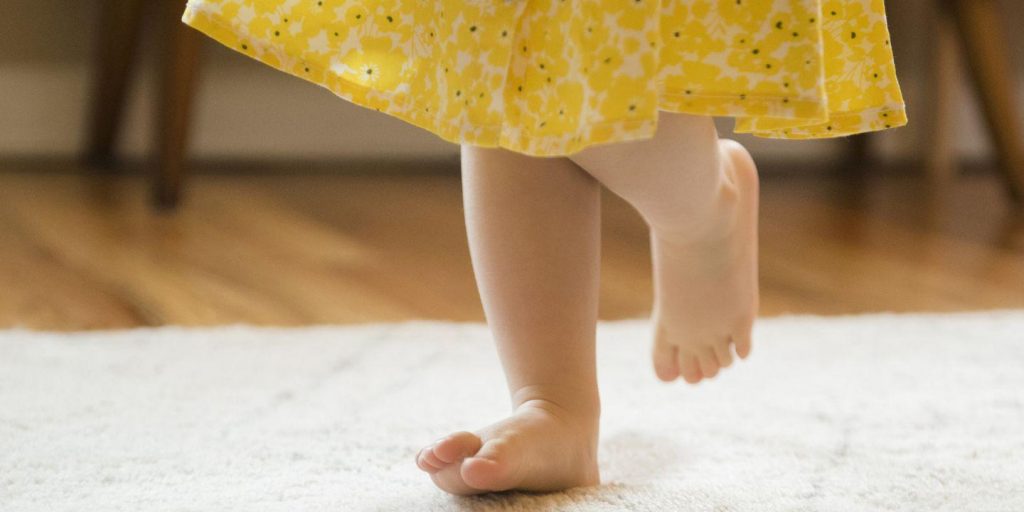در این تصویر پاهای کوچک یک دختربچه را می‌بینیم که بر روی فرش ماشینی اتاق کودک راه می‌رود. فرش اتاق کودک باید امنیت کودک را تأمین کند.